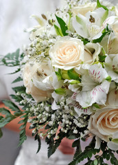 Bride holds elegant wedding bouquet of cream roses and lilies