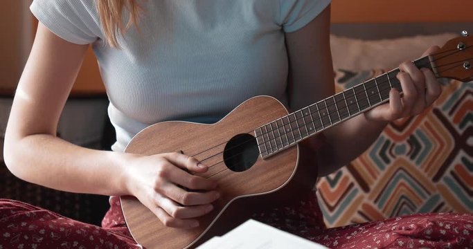 Girl plays musical instrument sitting at home. Ukulele strings. Camera - Canon 5D Mark IV