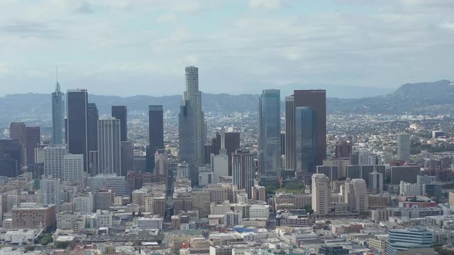 AERIAL: Slow Side Shot of Downtown Los Angeles Skyline with Warehouse Art Distrct in Foreground with Blue Sky and Clouds 