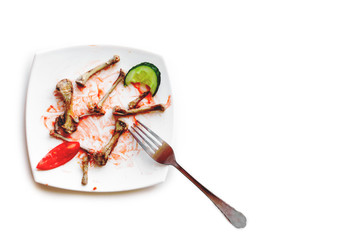 A white square plate with leftovers.Chicken bones on a plate fork tomato cucumber
