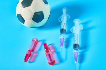 Football, soccer ball near syringe and ampoule on blue background. Concept of doping in professional sport. Rehabilitation, treatment after competition. Illegal medicaments using on tournament