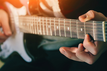 The musician plays an electric guitar, illuminated by bright sunlight, and holds the chords with...