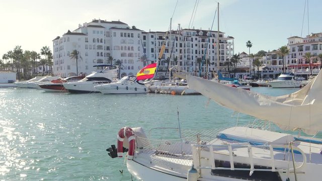 MANILVA, MALAGA / Spain - December 14 2019: Beautiful panoramic view of "Puerto de la Duquesa" Yachts and boats docked in the Harbour. Luxury Apartment Urbanisation.Spanish Flag. No camera movement