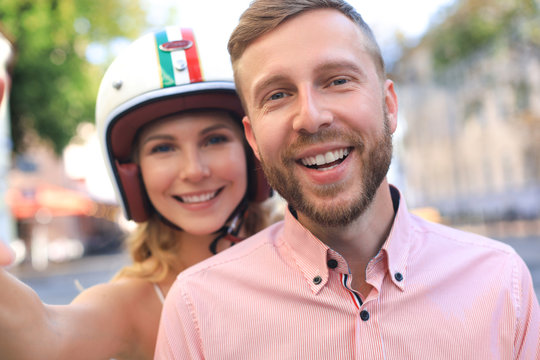 Happy young couple taking selfie while sitting on scooter outdoors.