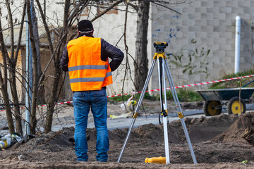 A craftsman is standing at a construction site near surveying equipment. A special device (level)...