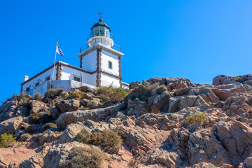 Fototapeta na wymiar Greek Lighthouse and Flag on a Sunny Cliff