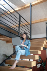 Young woman sitting on stairs, holding laptop on knees, typing