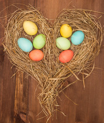 Fototapeta na wymiar Easter, and easter eggs in the heart. Easter eggs on a brown wooden table. Easter eggs and hay. Multi-colored eggs in a nest in the form of a heart.