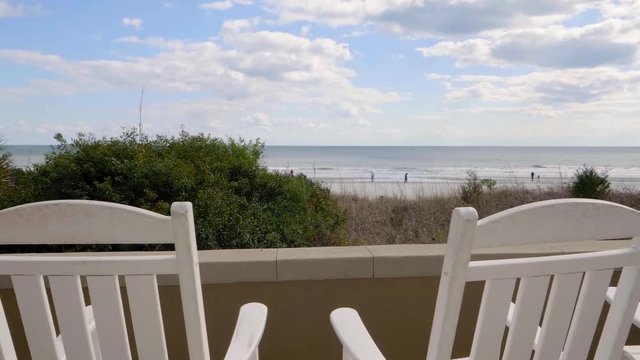 two empty white rocking chairs move gently on the veranda overlooking the ocean