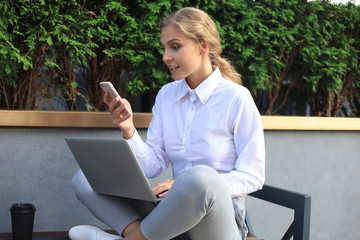 Happy entrepreneur working with a phone and laptop near the office.