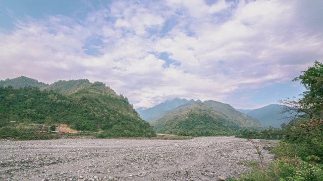 A beautiful scenic timelapse wide angle view of a nearly dried river with stone bed surrounded by hills and clouds passing by overhead, on a bright sunny day. Clear blue sky and clouds passing by.