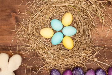 Fototapeta na wymiar Easter, Easter eggs collection as background. Easter eggs on a brown wooden table. Easter eggs and hay. Yellow and turquoise eggs in the nest.