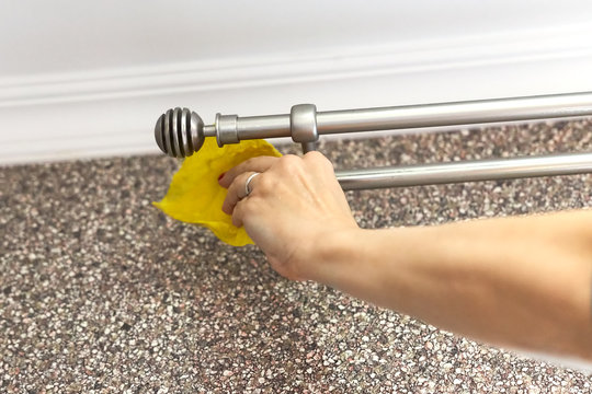 Woman washes a metal curtain rod with a yellow rag