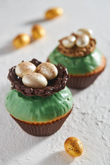 Delicious cupcakes decorated with glaze with a nest and eggs of chocolate on table