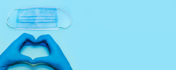 Blue medical mask on a blue background. Banner.Hand of a doctor in medical gloves depicts a heart gesture.Recovery, rescue, success! The concept of compliance with the quarantine regime, security