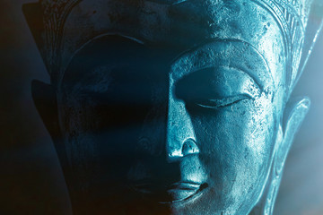 Spiritual enlightenment. Mindful Buddha face close-up with ethereal blue tone light.