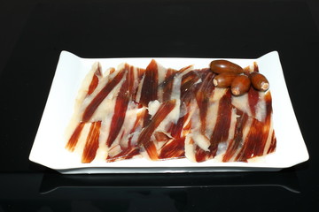 Iberian ham dish with acorns on black background