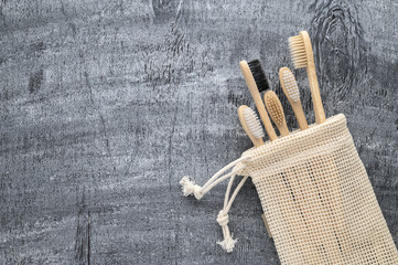 Zero waste concept. Set of eco natural bamboo toothbrushes in a cotton bag on a gray wooden background. Top view, copy space, horizontal orientation. Eco-friendly, no plastic.