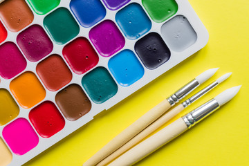 Creative layout with aquarelle palette, paint brushes on yellow background. Top view. Artists concept.
