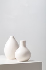 Closeup of two white clay vases on the table under the lights against a white background - obrazy, fototapety, plakaty