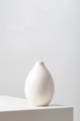 Vertical closeup of a white clay vase on the table under the lights against a white background - obrazy, fototapety, plakaty