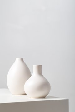 Closeup of two white clay vases on the table under the lights against a white background
