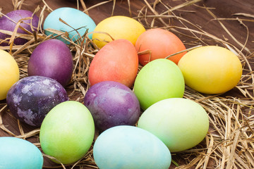 Fototapeta na wymiar Yellow, green, orange, biyuzovye and space eggs lie in the hay. Easter eggs and hay collection as a background. Multi-colored eggs in a row. Easter eggs on a brown wooden table.