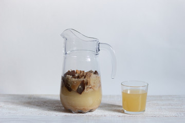 Homemade kvass with brown bread, yeast, sugar, water in  jug and glass on white background
