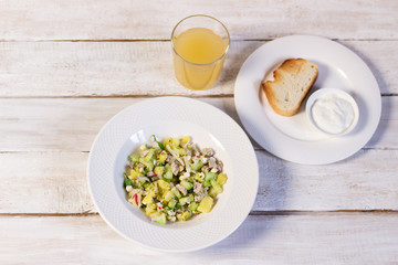 Cold soup okroshka with homemade kvass, sour cream in white plate, bread on rustic background