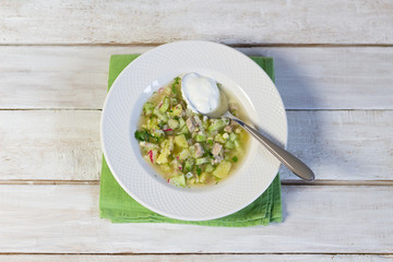 Cold soup okroshka with homemade kvass, sour cream in white plate on rustic background