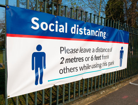 Large banner attached to railings, warning the general public to keep to the social distancing rules whilst using the public parks, in the London Borough of Bexley.