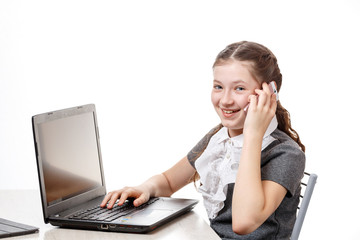 Cute schoolgirl sitting at a laptop and talking on the phone on a white background