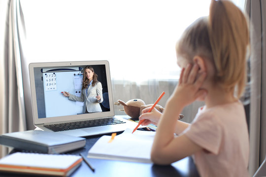 Distance learning. Cheerful little girl using laptop computer studying through online e-learning system.