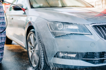 Woman washing car at car wash station using high pressure water machine.