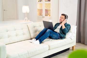 male listens audio with headphones on sofa