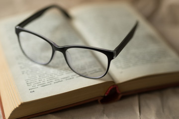 Black glasses lie on an open book, reading, sight, leisure, hobby
