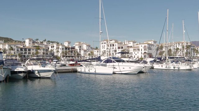 MANILVA, MALAGA / Spain - December 14 2019: Beautiful panoramic view of "Puerto de la Duquesa" Yachts and boats docked in the Harbour. Luxury Apartment Urbanisation and Restaurants. Camera Pan Right