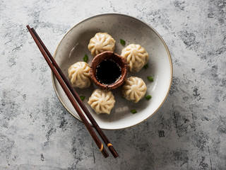   Chinese steamed dumplings in a plate with soy sauce and chopsticks on a gray concrete background top view