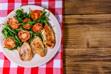 Roasted chicken breasts and salad with arugula and cherry tomatoes in a ceramic plate. Top view