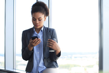 Attractive african american business woman using mobile phone while standing in creative office.