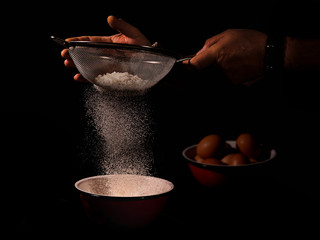 Persona colando harina para hacer bollos con una cesta de huevos