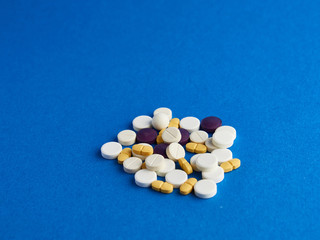 Side view of yellow, white and purple pills on a blue background.