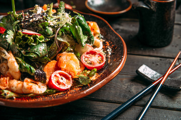 Closeup on appetizing delicious seafood salad with vegetables on the clay plate on the wooden table with chopsticks, horizontal format