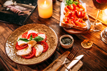 Fototapeta na wymiar Wooden table served with appetizing italian cuisine dishes caprese salad with tomatoes with mozzarella cheese and prosciutto bruschettas, horizontal format