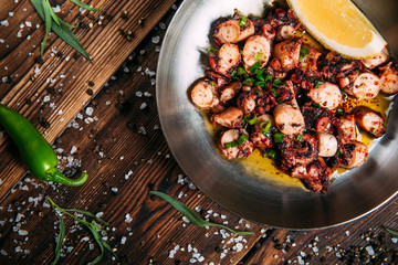 Top view on appetizing fried chopped octopus tentacles with lemon in a pan on the wooden table, horizontal format