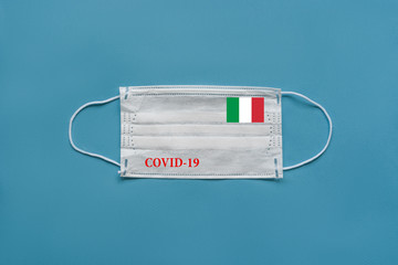 Medical mask with the flag of Italy and the inscription COVID-19 on a blue background