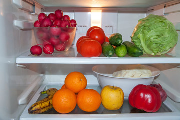 refrigerator full of fresh raw fruit and vegetables,pine apple,parsley,dill,lemon,pepper,oranges,apple,banana,green cabbage,cucumbers,red tomatoes,redish,ginger