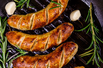Roasted sausages with rosemary twigs and garlic in a cast iron grill pan. Top view