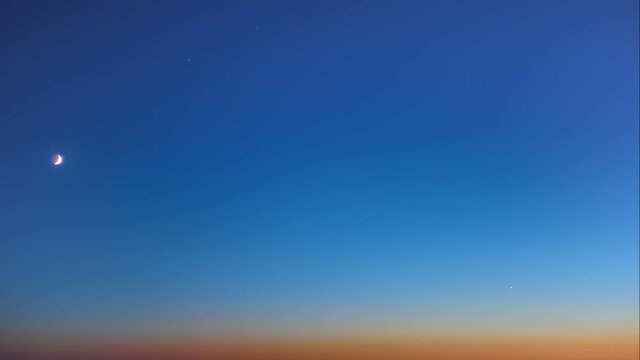 Aerial panoramic time lapse of the crescent moon and star descending towards the horizon in a dark blue sky in the twilight after sunset 