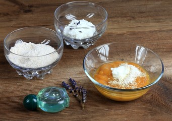 Homemade face mask from mango, heavy cream and finely ground oats. Three bowls full of food ingredients and lavender oil on the brown table.